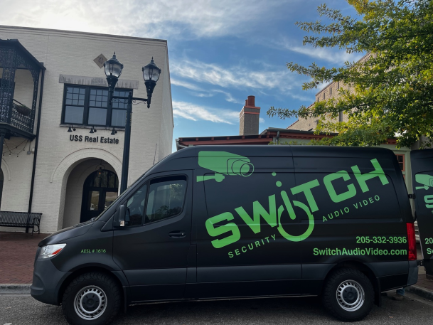 Black service van featuring a bright green "SWITCH" logo parked in front of a multi-story building on a sunny day.
