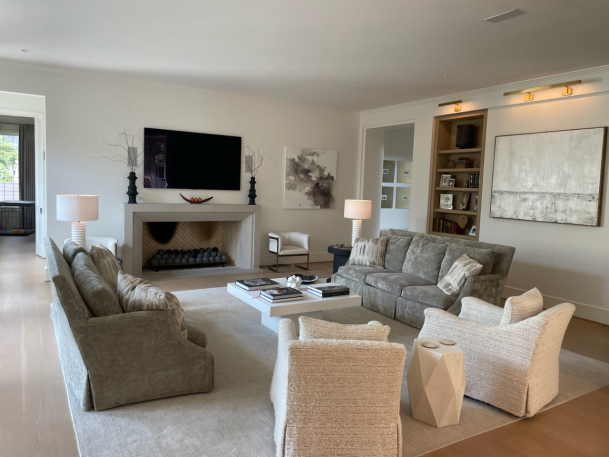 Spacious, airy living room featuring neutral tone furniture, a central fireplace, a mounted TV, and large windows.