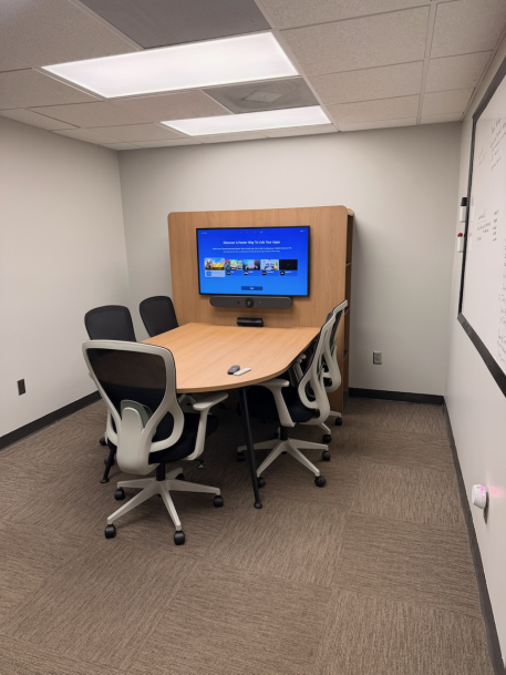 Small conference featuring a light wood desk, office chairs, and a wall-mounted TV display.