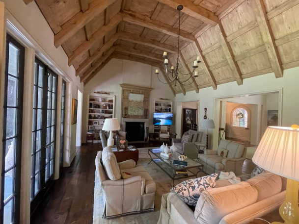 High-angled view of a great room featuring vaulted wood-plank ceilings, tall windows, chandeliers, and neutral furnishings.