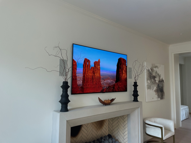 Wall-mounted TV displaying a red rock landscape above a sleek white fireplace mantle.