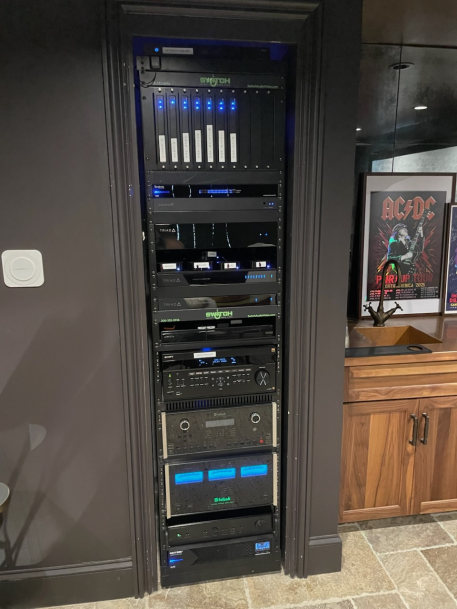 Tall, custom AV audio-visual equipment rack neatly built into a dark wall alcove next to a wooden cabinet.