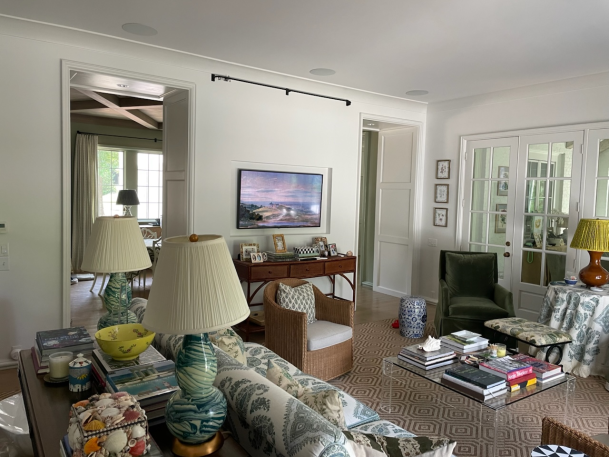 Elegantly decorated living space with patterned upholstery, vibrant lamps, artwork, and view into an adjacent room with a mounted TV.
