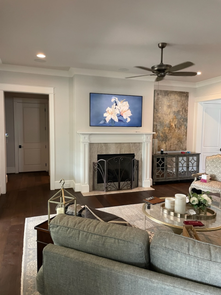 Bright living room with light walls, a ceiling fan, a fireplace topped with artwork, and comfortable sofa seating.